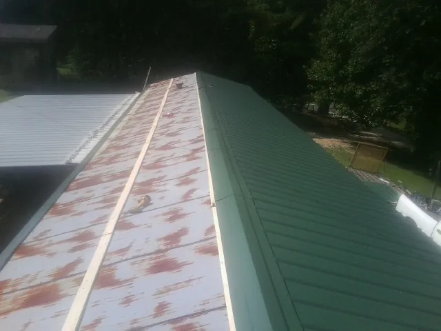 Old rusted panels beside newly installed green metal roofing — Wind Damage Roof Repair by Roofing Brothers in Port Royal