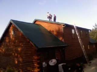 Crew on the ridge of a green metal roof on a two story log home in Port Royal